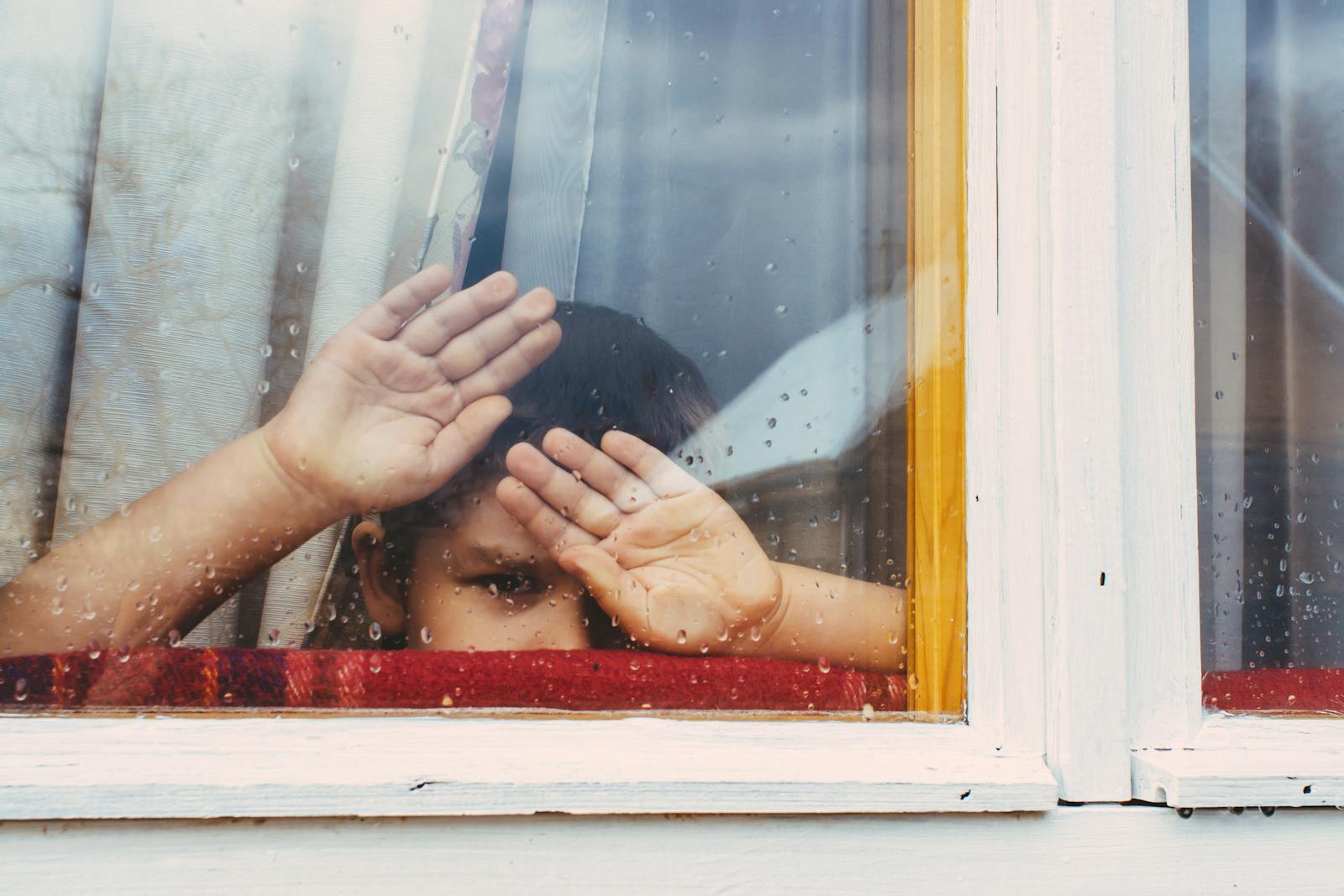 Boy looking through a rain-speckled window