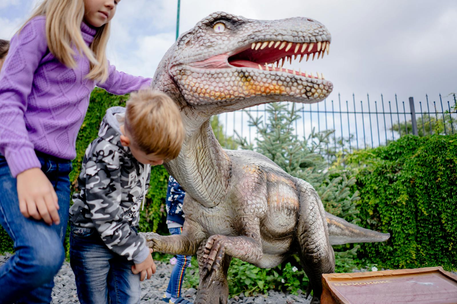 Children playing around an outdoor dinosaur statue at a museum