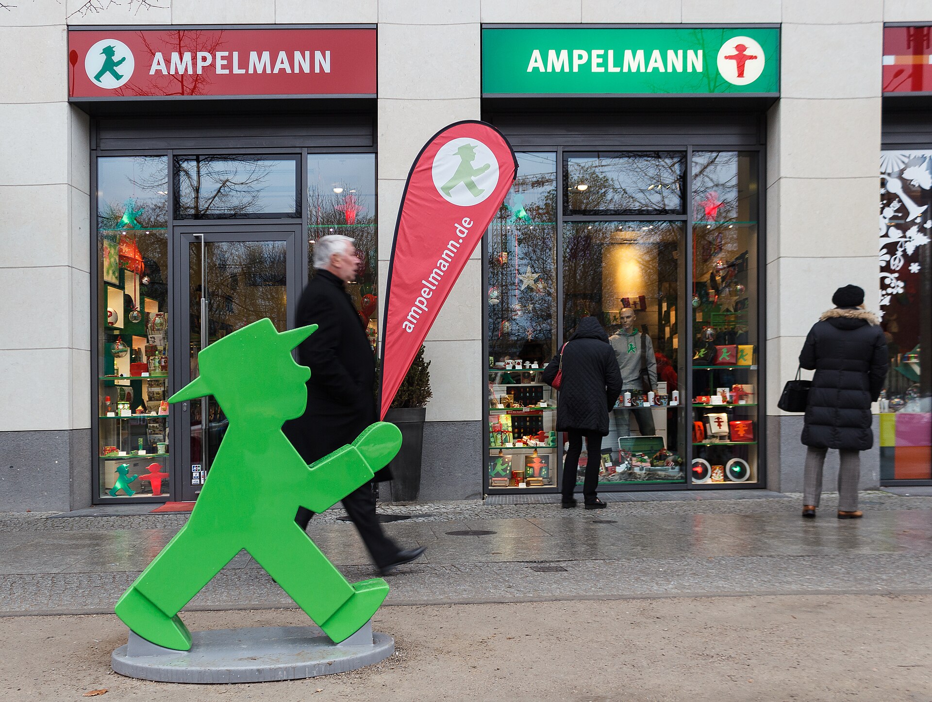 The front of an Ampelmann shop in Berlin, with red and green Ampelmann signs above the windows and a large green Ampelmann figure on the pavement outside
