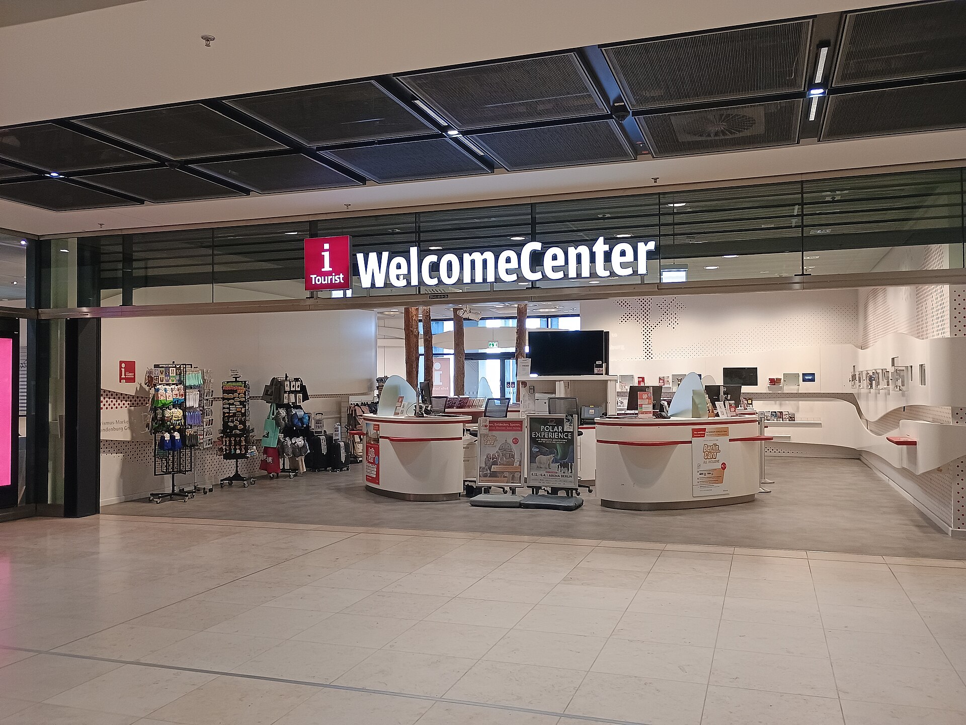 The Berlin Brandenburg WelcomeCenter tourist information office in BER Terminal 1, with its illuminated sign, counters and racks of souvenirs and brochures