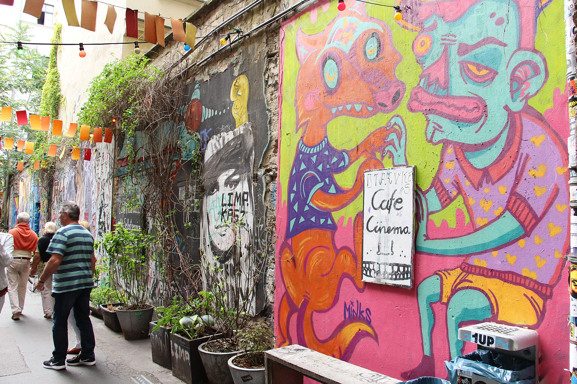 A narrow courtyard alley at Haus Schwarzenberg in Mitte, its walls covered in colourful murals and paste-ups, with pot plants, bunting and a Café Cinema sign