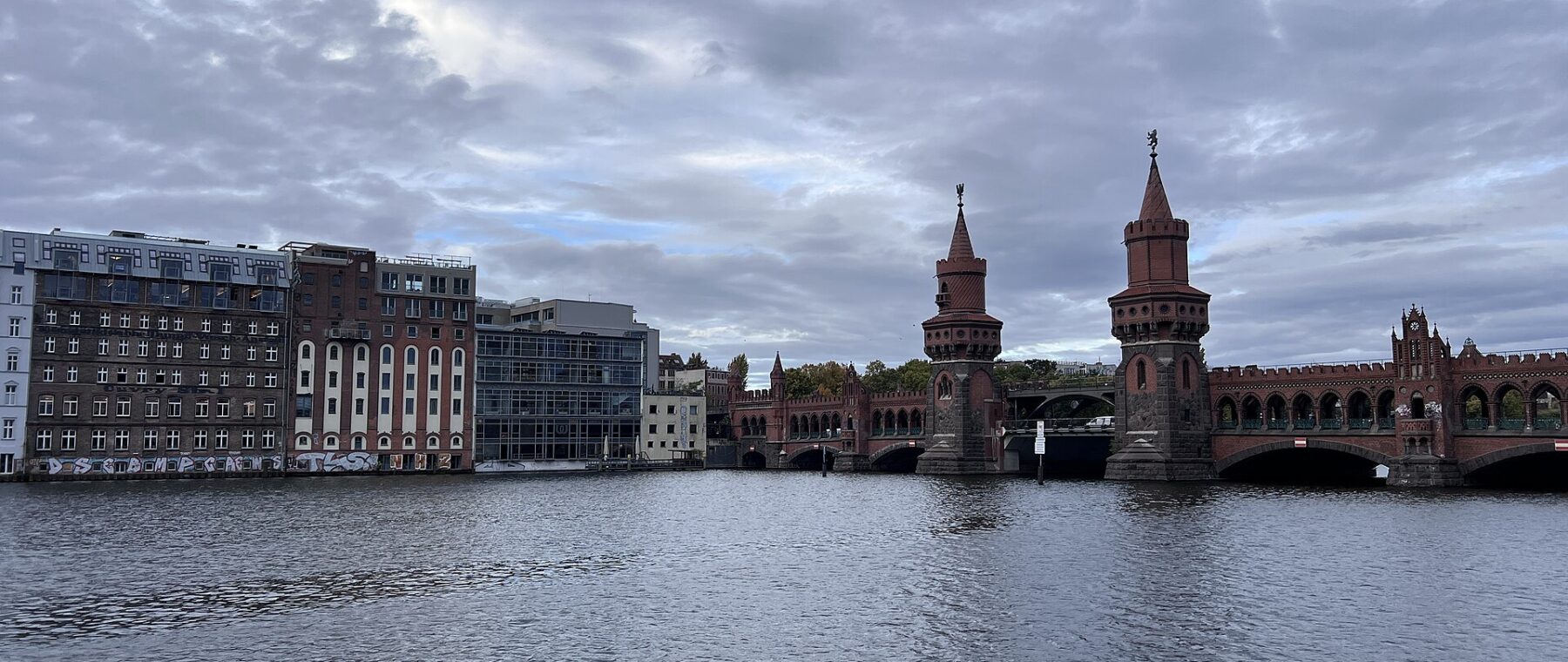 The twin brick towers of the Oberbaumbrücke seen across the Spree under a cloudy Berlin sky