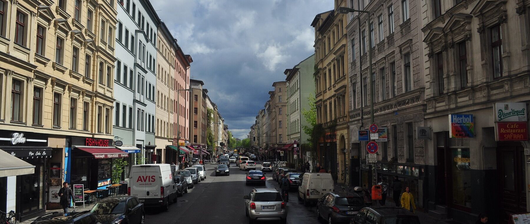 Oranienstraße in Kreuzberg with shopfronts and parked cars under a stormy sky