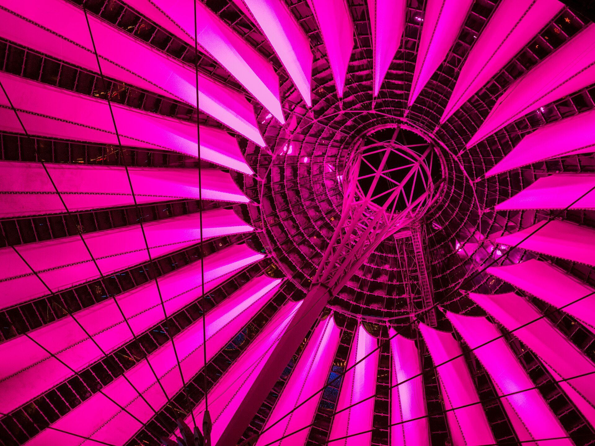 The illuminated fabric and steel roof of the Sony Center at Potsdamer Platz in Berlin glowing magenta at night