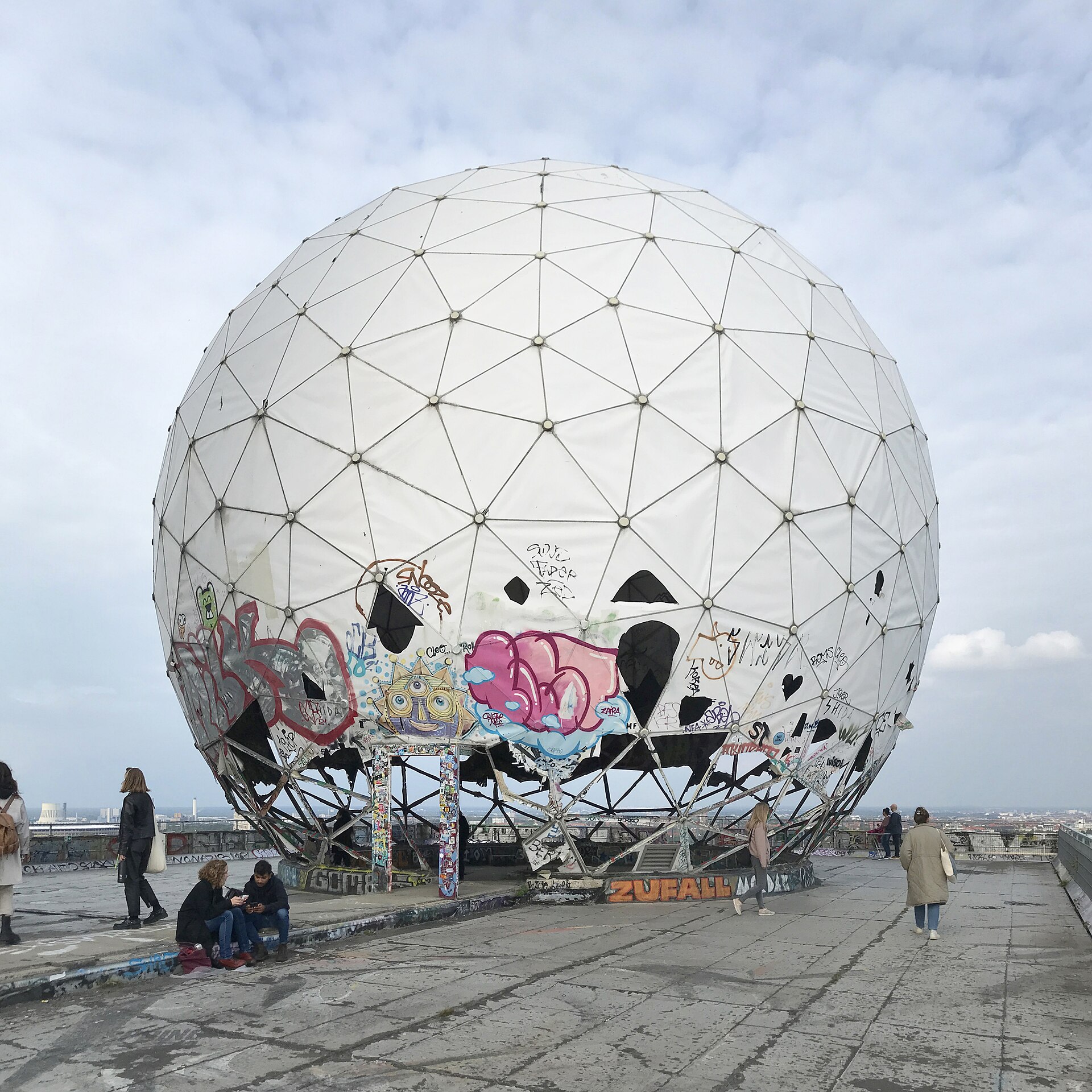Graffitied white geodesic radome at the abandoned Teufelsberg listening station with visitors on the concrete roof